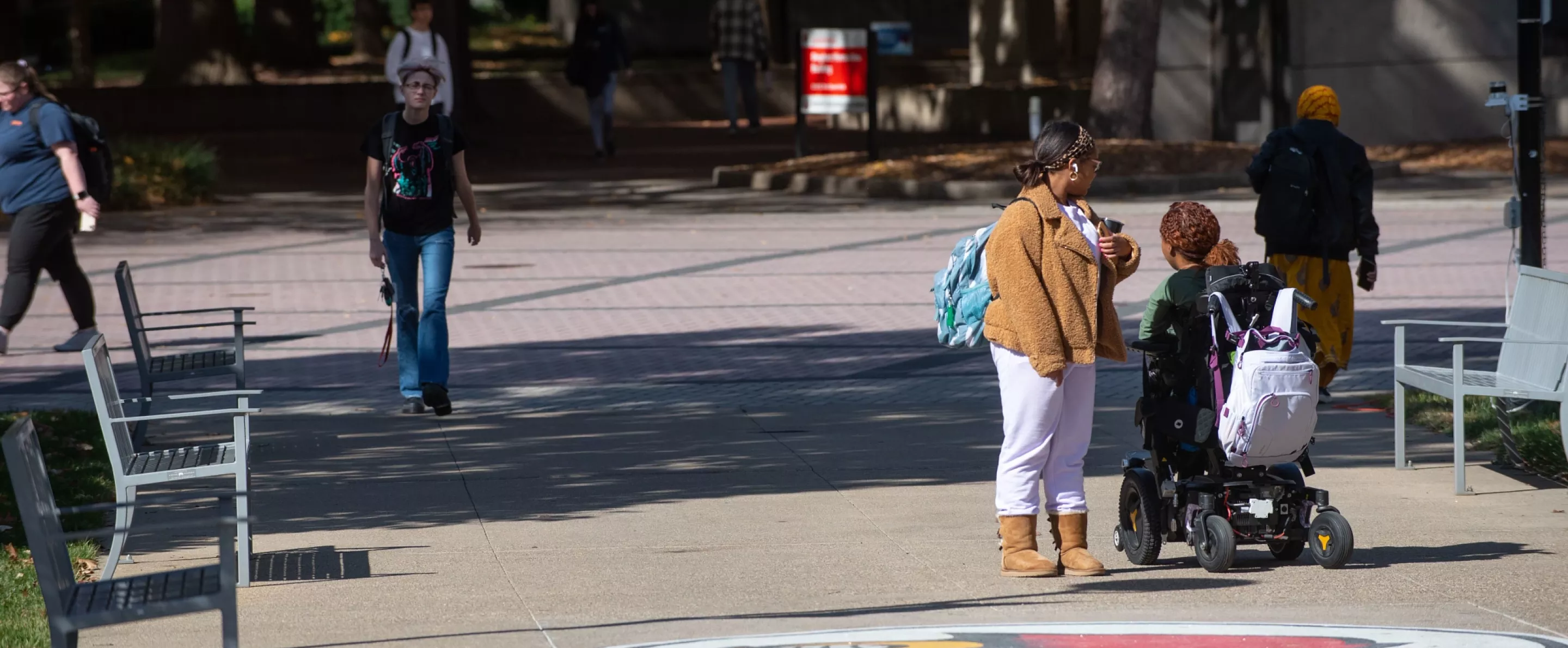 Students walk around campus and a student in a motorized wheelchair makes way towards the Bingham Humanities Building.